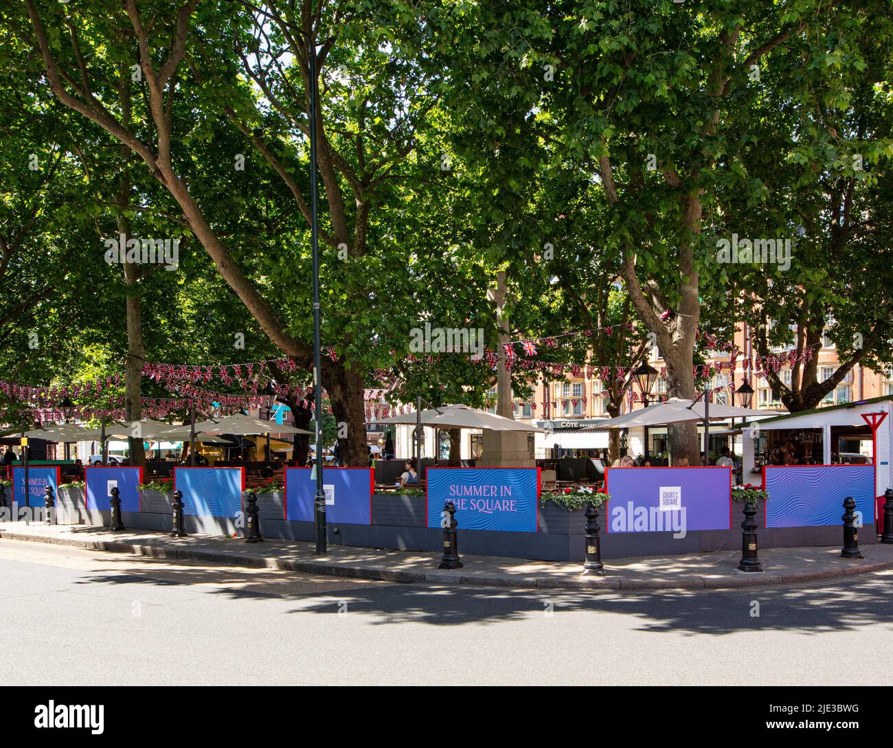 Sloane Square, Chelsea, London, Sommer 2022; Banner für Feierlichkeiten in der Mitte des von Bäumen gesäumten Platzes Stockfoto
