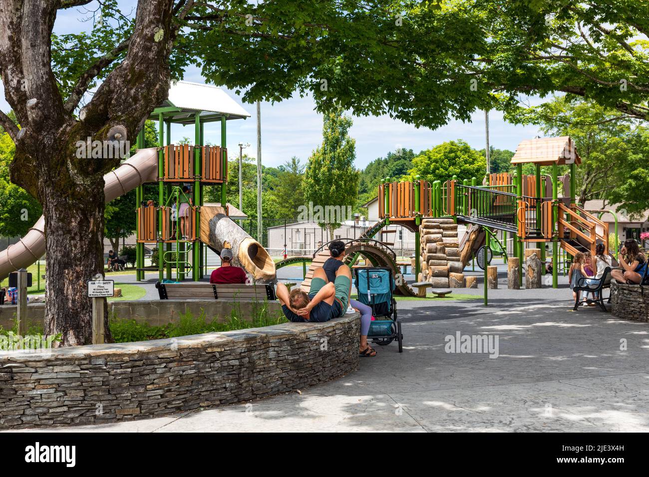 BLOWING ROCK, NC, USA-20 JUNE 2022: Blowing Rock City Park, Erwachsene entspannen sich, während Kinder spielen, rutschen und klettern auf mehreren bunten Spielplatzstrukturen Stockfoto