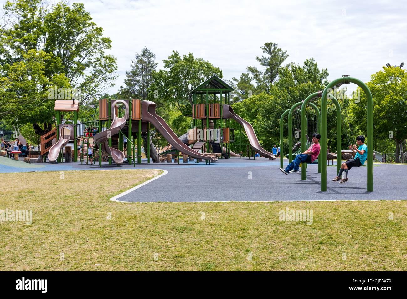 BLOWING ROCK, NC, USA-20 JUNE 2022: Spielplatz im City Park spielen zwei Jungen auf Schaukeln, Spielgeräten und Kindern im Hintergrund. Stockfoto