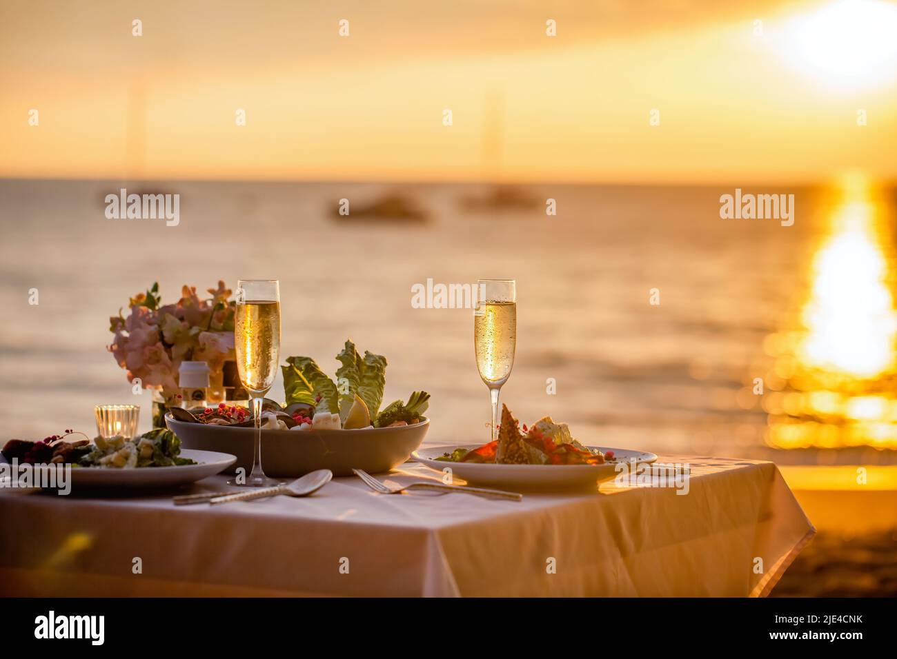 Romantisches Abendessen bei Sonnenuntergang am Strand. Tischset für zwei Personen mit luxuriösem Essen, Gläser Champagner-Getränke in einem Restaurant mit Meerblick. Sommerliebe Stockfoto