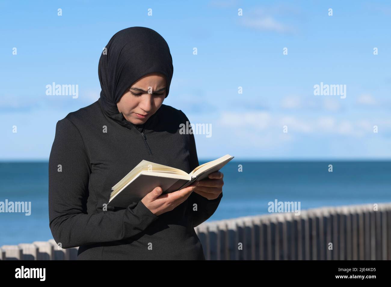 Fokussierte muslimische Frau, die im Freien ein Buch liest Stockfoto