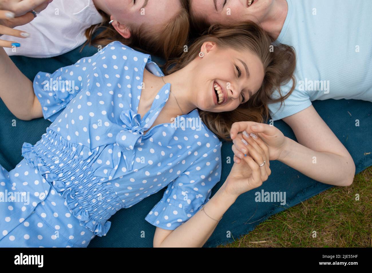 Lachende junge Mädchen, die auf einer blauen Decke auf grünem Gras liegen und die Hände aus der Nähe halten. Spaß haben und glückliche Momente im Freien genießen. Mädchen Stockfoto