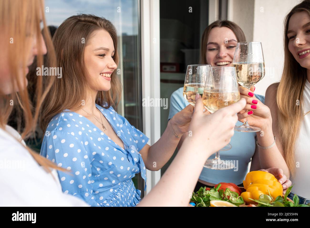 Fröhliche junge Frauen stehen auf der Terrasse zusammen, klirren Gläser und trinken Wein aus der Nähe. Spaß haben und Erholung im Freien genießen. Mädchenparty Stockfoto