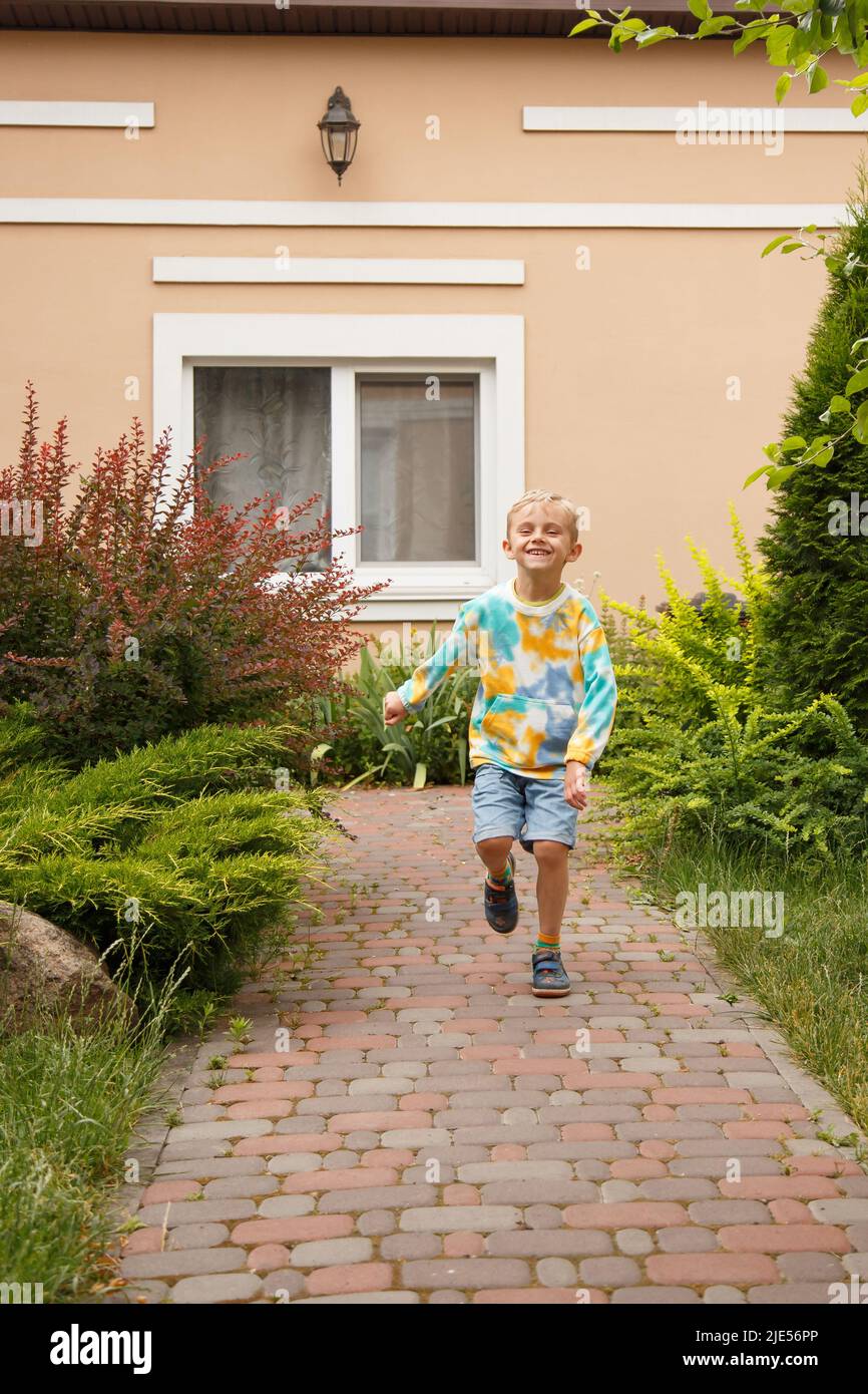 Ein Junge mit europäischem Aussehen geht fröhlich, ein fünfjähriger Junge geht den Weg entlang. Stockfoto