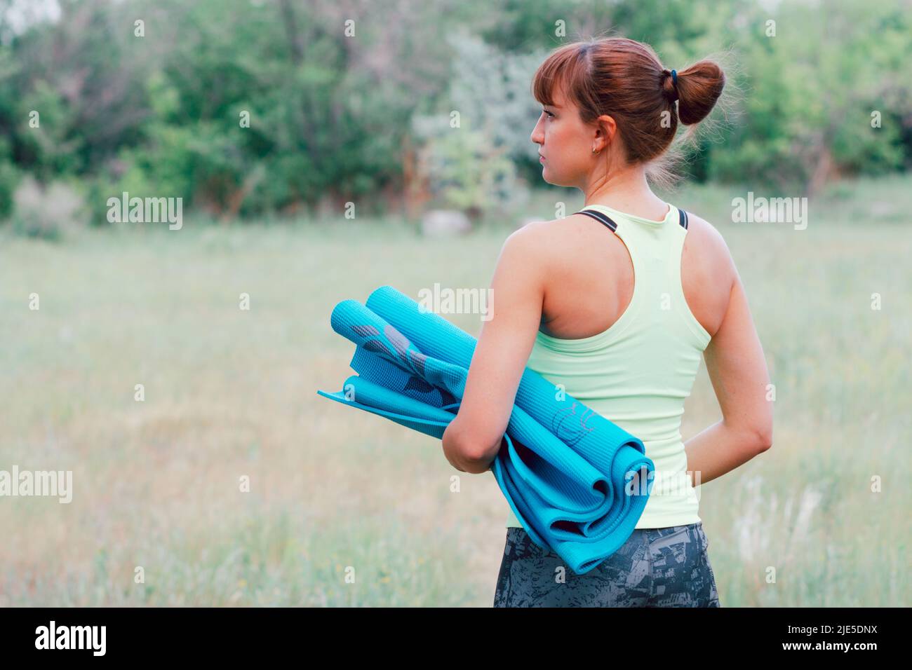 Junge schlanke Frau in Sportkleidung mit Yogamatte, während sie zum Training im Freien geht Stockfoto