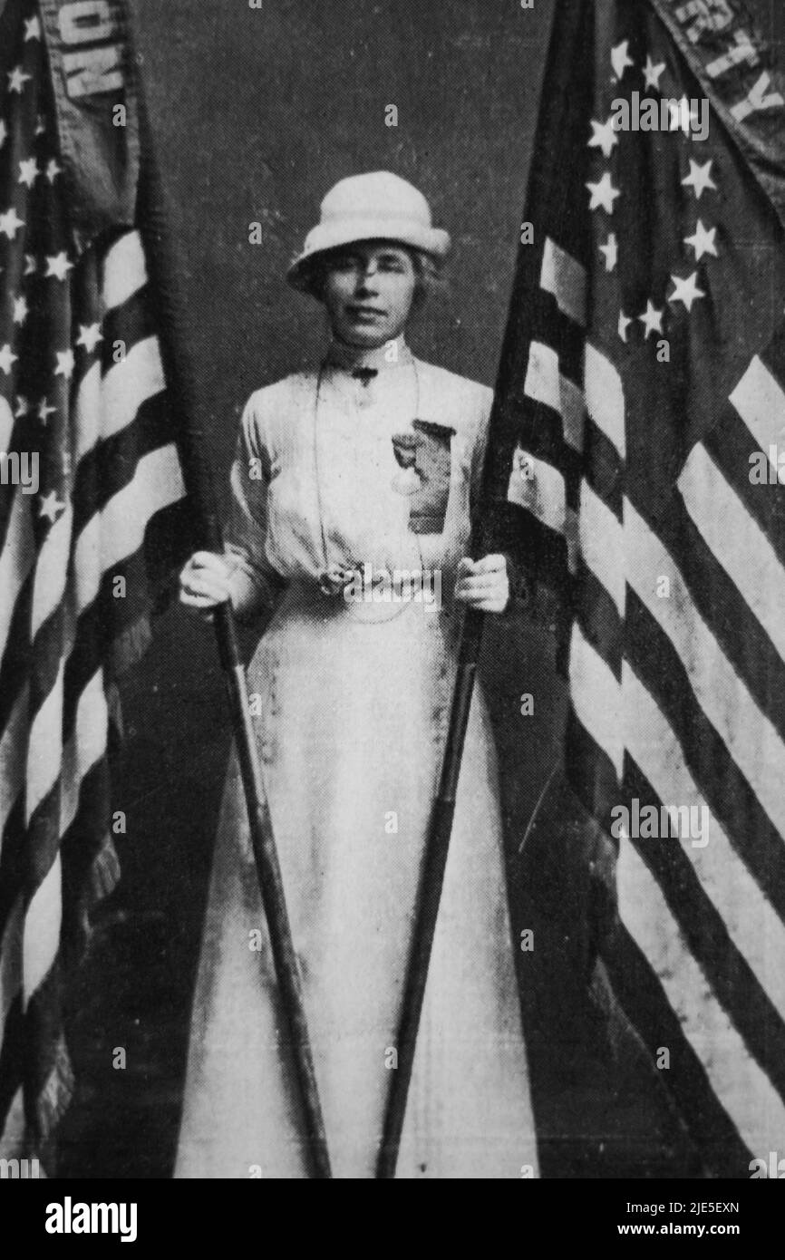 Eine Frau, die ihr Sonntagskleid und ihren Hut trägt, während sie zwei Flaggen von Betsy Ross für die Vereinigten Staaten von Amerika hält. Stockfoto