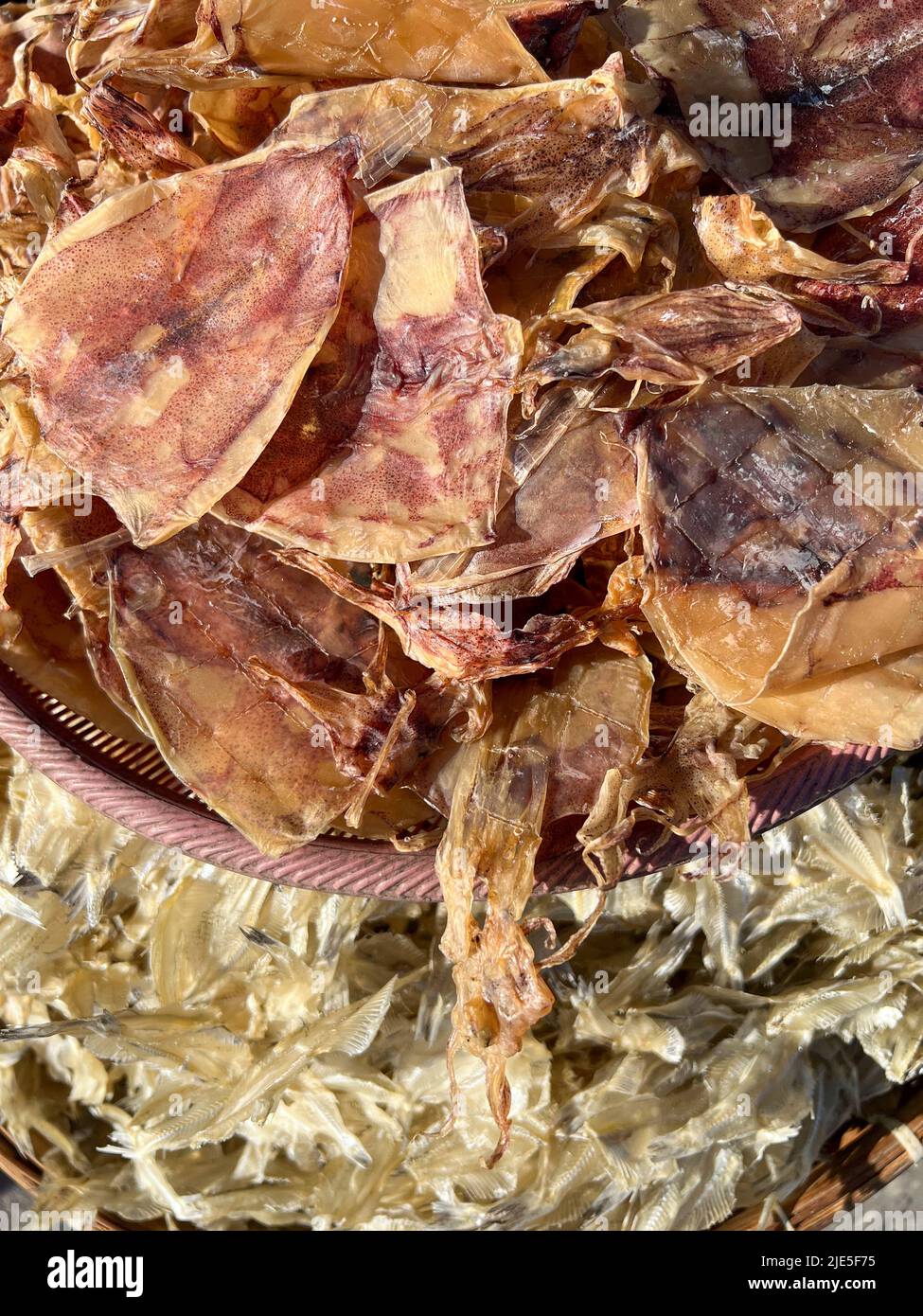 Getrocknete Meeresfrüchte wie getrockneter Tintenfisch, getrockneter weißer Fisch im Bambuskorb, unter Sonnenlicht auf dem Markt Stockfoto