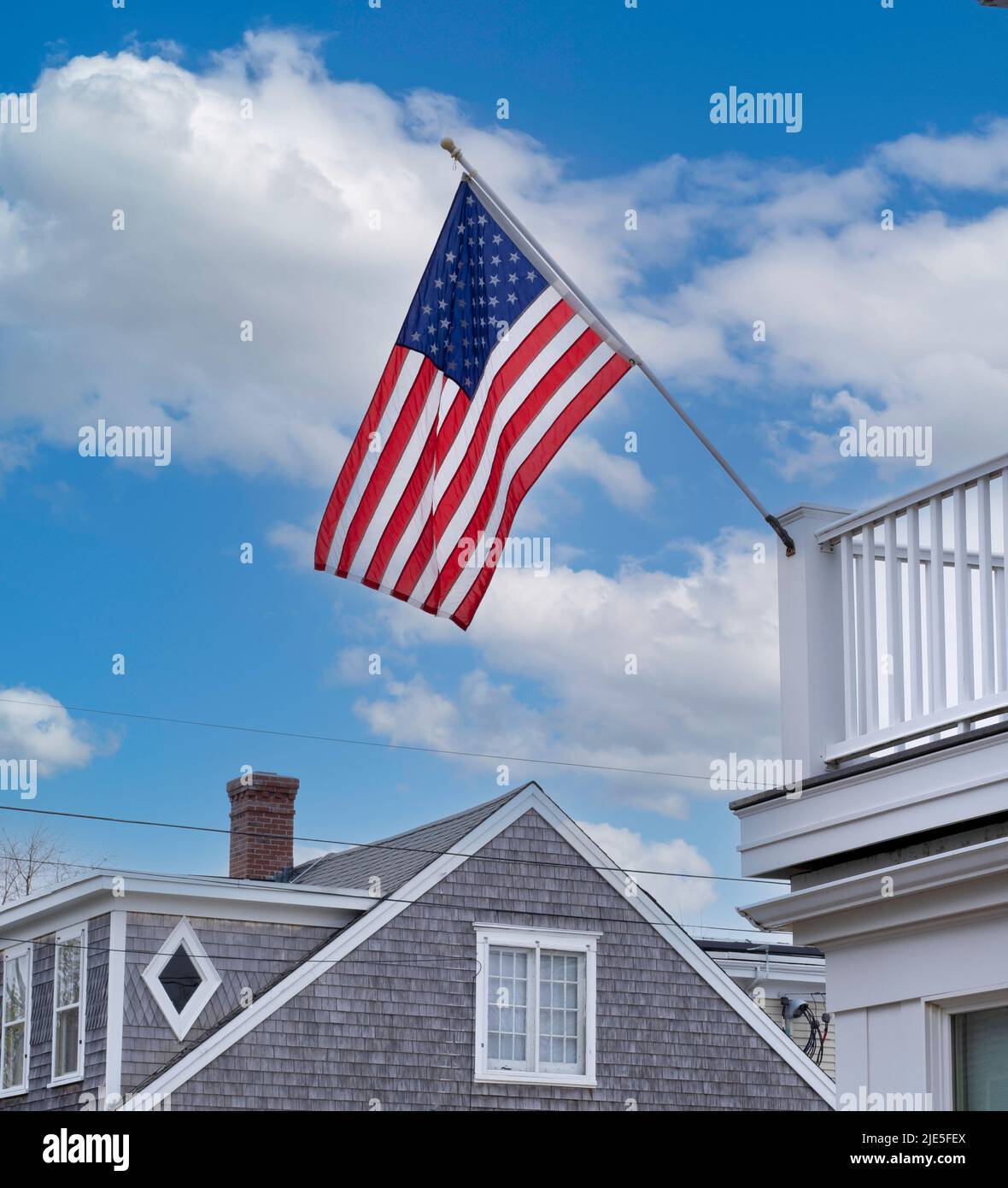 Vereinigte Staaten von Amerika Flagge gegen blauen Himmel mit Wolken, die an der Stange an der weißen Deckgeländer auf dem Dach des Hauses auf Cape Cod hängen Stockfoto