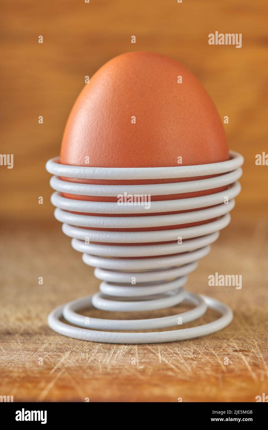 Ein gekochtes Ei in einer spiralförmigen Metallstütze auf Holzhintergrund Stockfoto