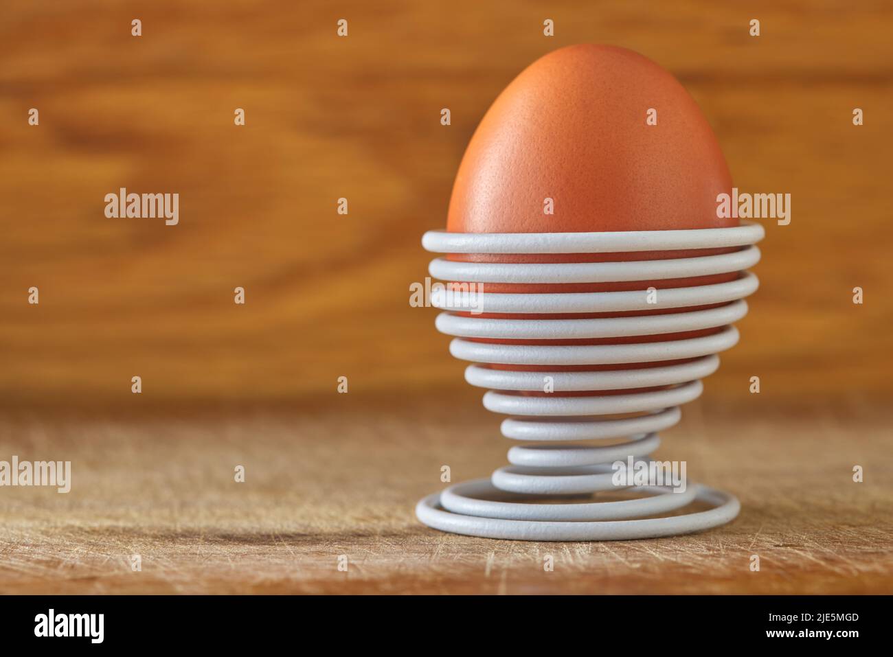 Ein gekochtes Ei in einer spiralförmigen weißen Metallstütze auf Holzhintergrund mit Kopierraum Stockfoto
