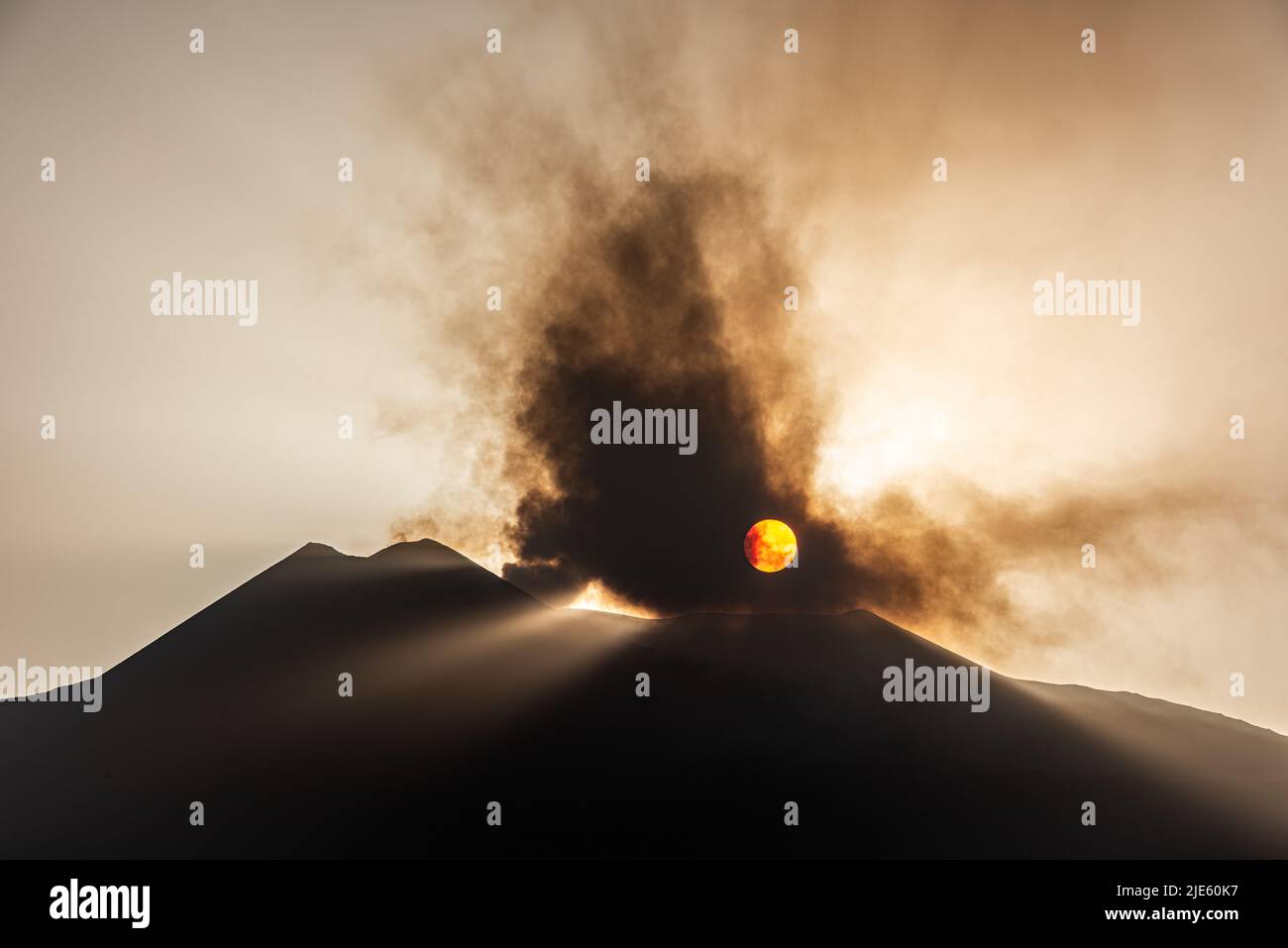 Die untergehende Sonne, die durch eine Wolke vulkanischer Asche vom Ätna auf Sizilien, dem aktivsten Vulkan Europas, ausbricht Stockfoto