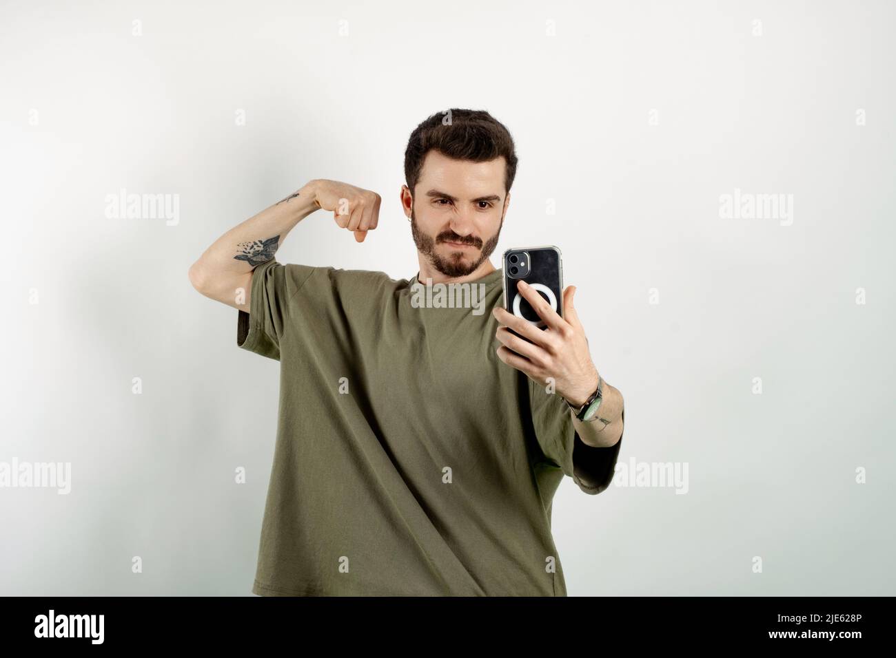 Hübscher junger Mann in legerer Kleidung posiert isoliert auf weißem Hintergrund und macht Selfie, zeigt starken Arm, beugt Bizeps und posiert für Fotos Stockfoto