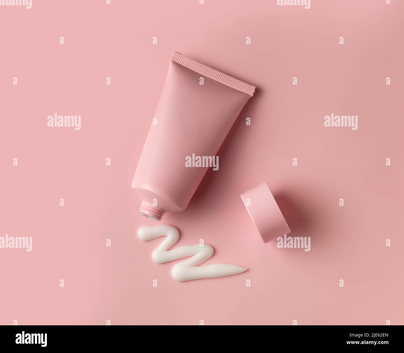 Saubere Gesichts-Körper-Creme-Tube von rosa Farbe mit offener Kappe und Produkt gequetscht Creme Textur auf Fleisch Farbe Hintergrund Stockfoto