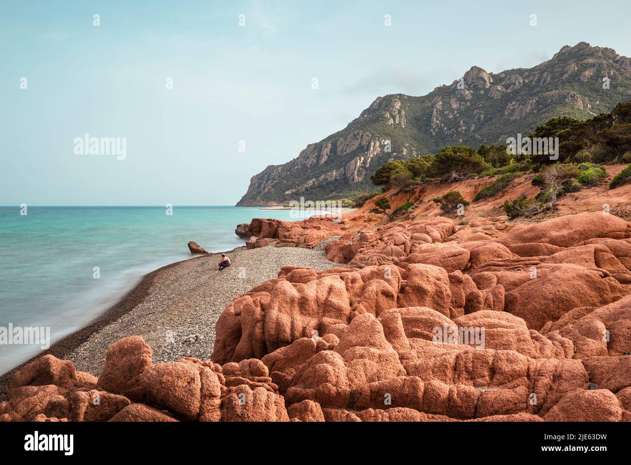 Der graue Kiesstrand Coccorocci, eingerahmt von roten Porphyrfelsen, und die Wälder rund um den Monte Cartucceddu an der Ostküste Sardiniens, Ogliastra, Italien Stockfoto