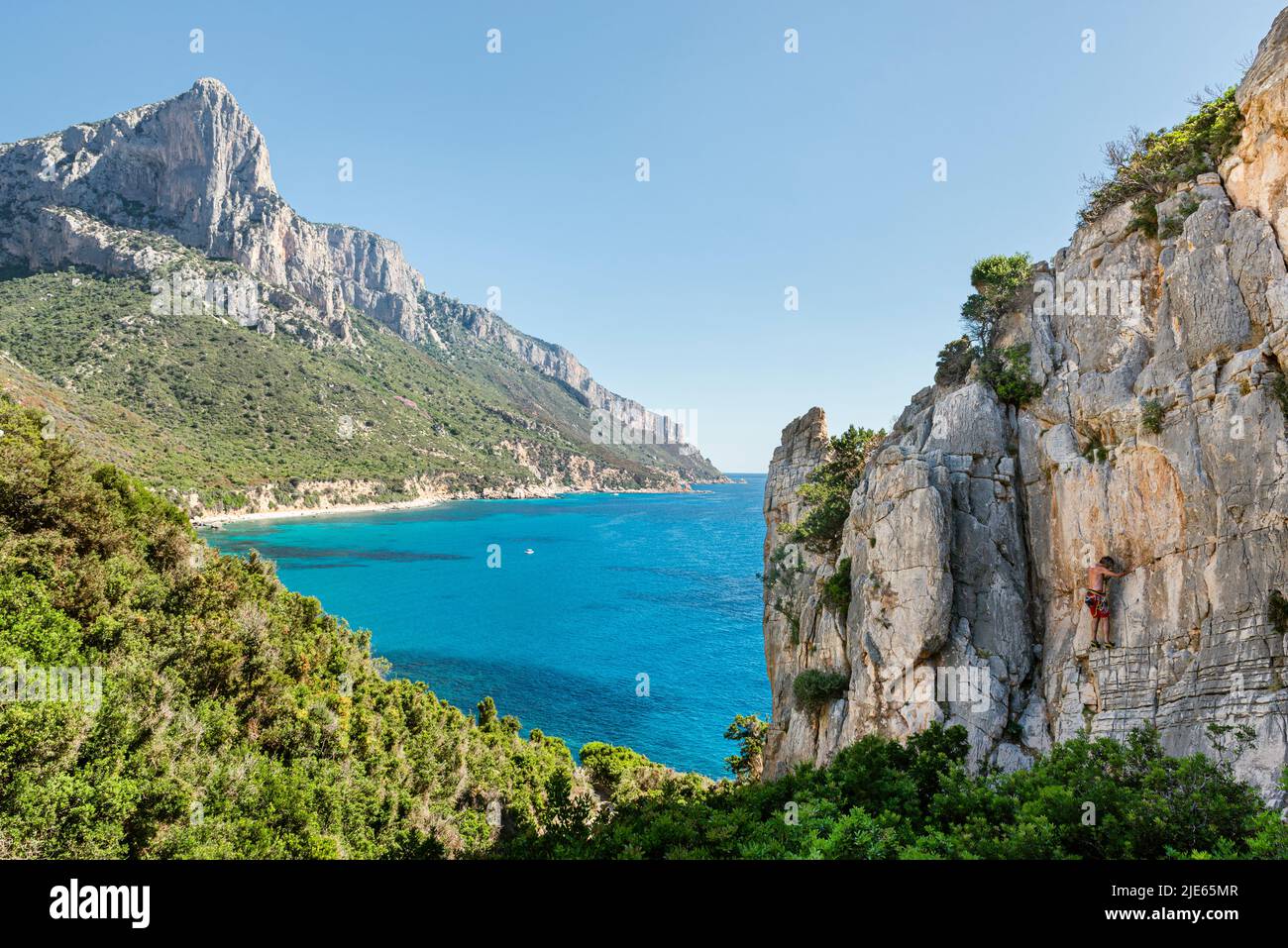 Ein Bergsteiger auf den Felsen von Pedra Longa mit Blick auf die felsigen Klippen von Punta Giradili über dem türkisfarbenen Meer an der Ostküste Sardiniens, Italien Stockfoto