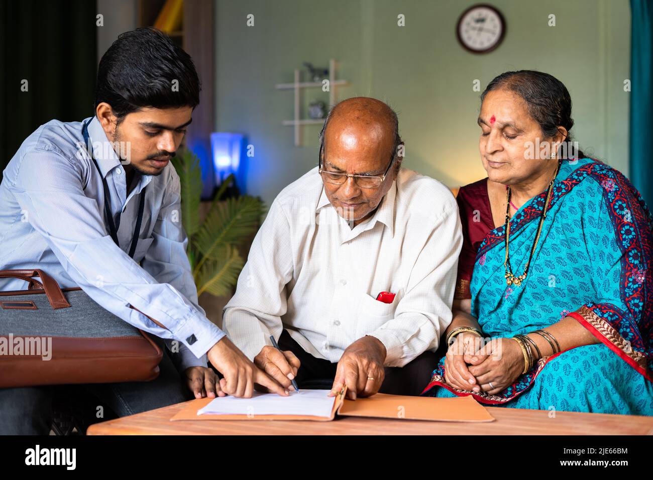 Seniorenpaar unterzeichnet Versicherungsdokumente vom Bankbeamten zu Hause - Konzepte der finanziellen Unterstützung, Banken und Investitionen Stockfoto