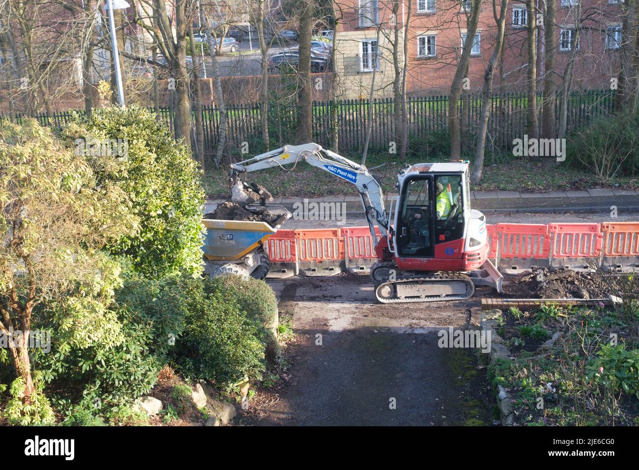 Arbeiter, der einen Minibagger benutzt, um einen Bürgersteig an einer Straße in einem Wohngebiet zu graben Stockfoto