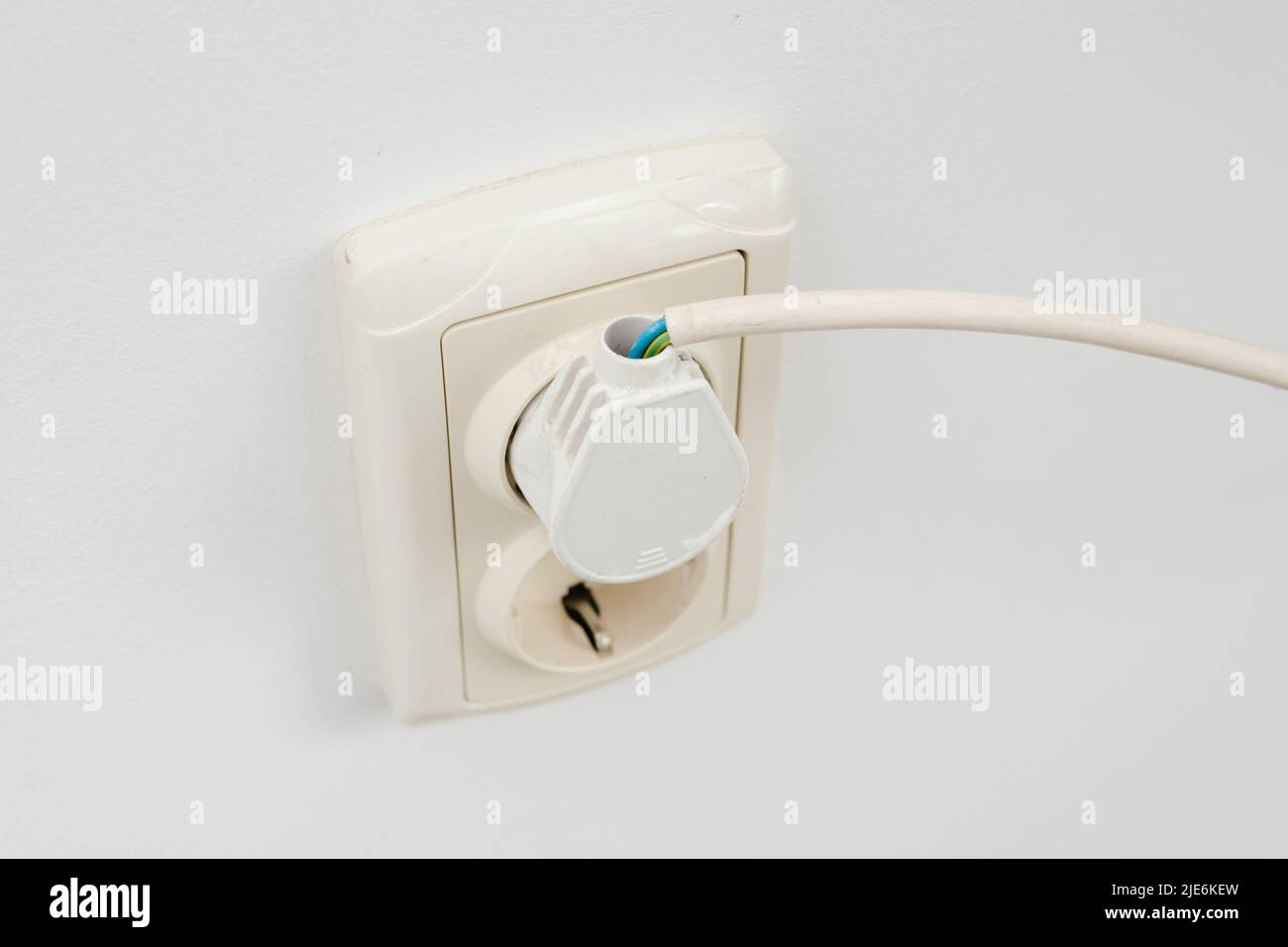 Beschädigte Isolierung des Stromkabels in der Steckdose eines Heizkessels gegen eine weiße Wand. Stockfoto