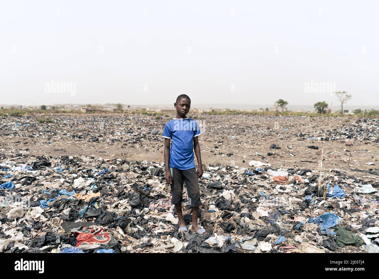 Kleiner afrikanischer Junge, der auf einem mit Müll bedeckten Feld steht; Misswirtschaft bei Abfällen in Entwicklungsländern Stockfoto