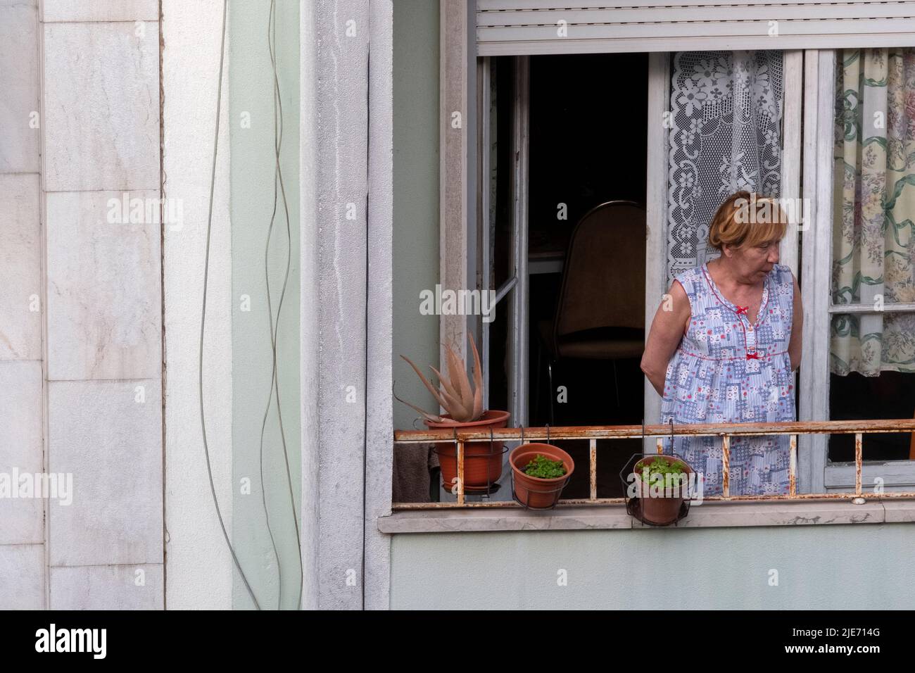 Ältere Frau, die von ihrer Wohnung in Lissabon, Portugal, aus den Blick auf die Straße schaut Stockfoto