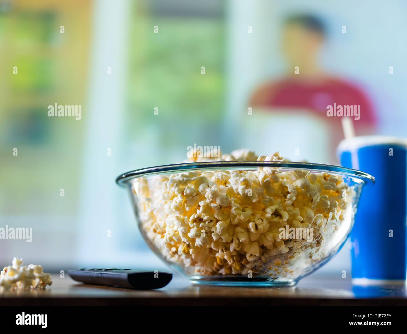 Ein klassisches Set eines Sportfans - eine Schüssel Popcorn, ein Limonade-Getränk und eine TV-Fernbedienung vor dem Hintergrund eines Fernsehers mit einem Fußballspiel und einem Fenster. Wat Stockfoto