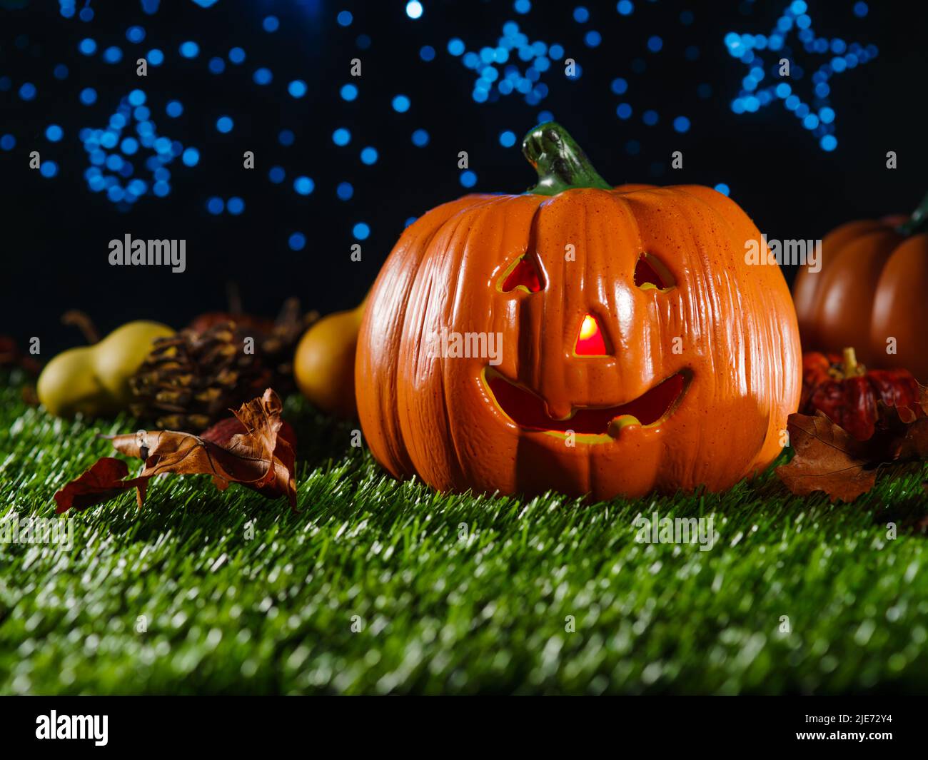 Mystische Komposition. Auf dem grünen Gras, einem orangefarbenen Kürbis, Herbstfrüchten und Zapfen vor einem dunkelblauen Sternenhimmel. Halloween-Feier. Banner, in Stockfoto
