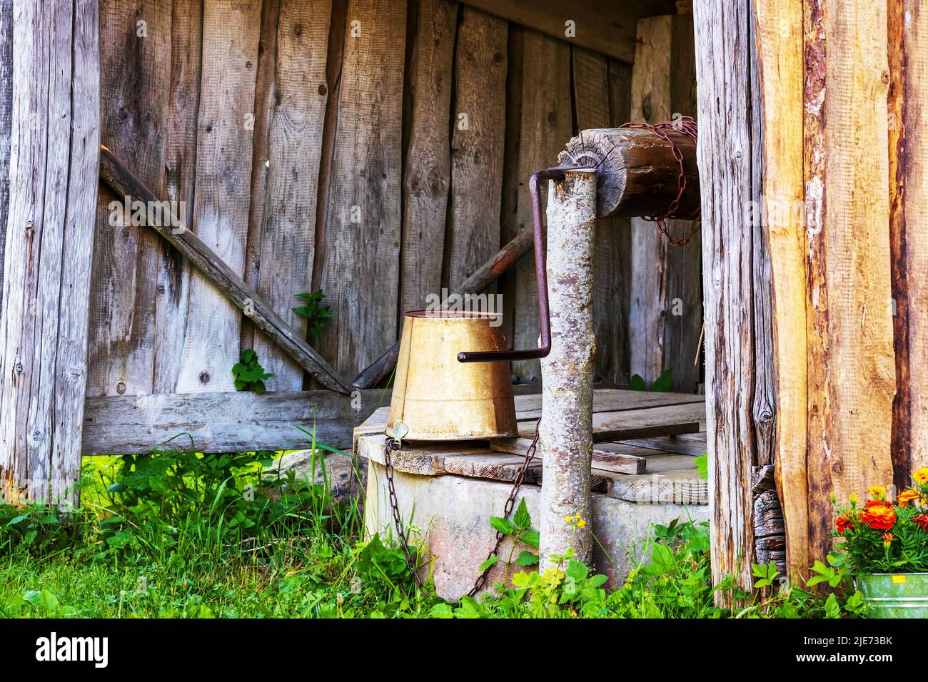 Ein alter Brunnen mit einem hölzernen Baldachin und einem Metalleimer in einem europäischen Dorf Stockfoto