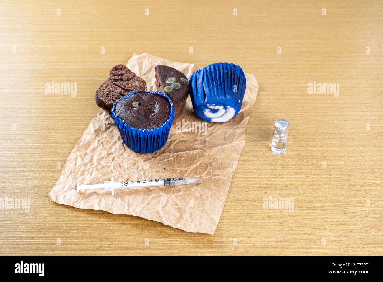 Spritze mit Insulin neben alten, schimmeligen Muffins. Stockfoto