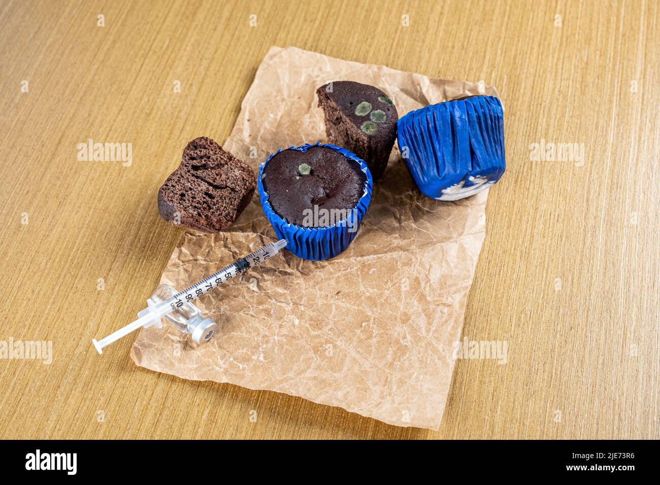 Spritze, die Insulin in schimmeligen Schokoladenmuffin injiziert. Stockfoto