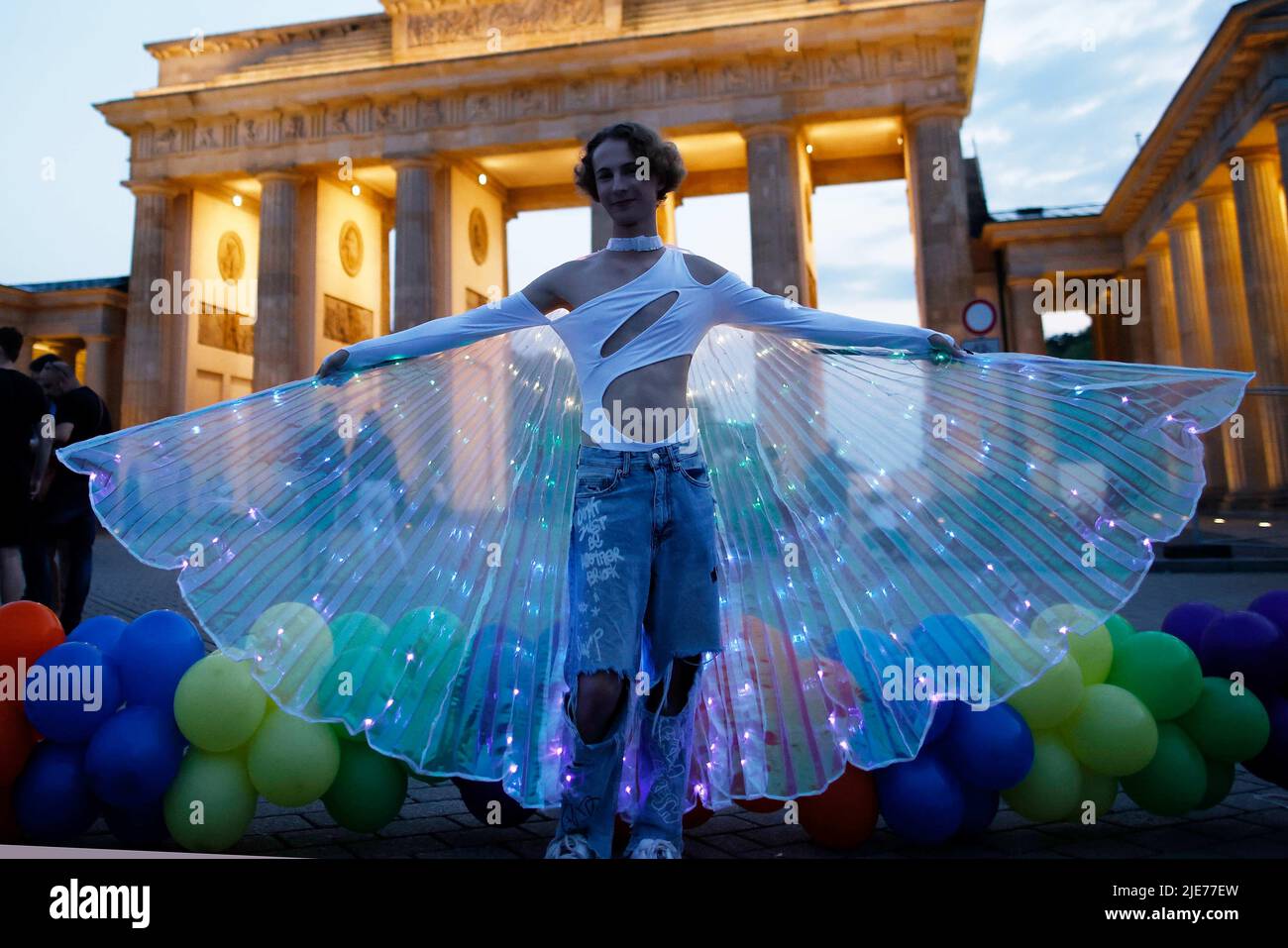 Berlin, Deutschland. 25.. Juni 2022. Ein Teilnehmer trägt einen leuchtenden Umhang an einer Gedenkstätte für die Opfer des Angriffs in Oslo am Brandenburger Tor. Im Zentrum der norwegischen Hauptstadt hatte am Samstagabend ein mutmaßlicher Einzelschütze auf andere Menschen in und um eine Schwulenbar geschossen. Der Akt mit zwei Todesopfern und mindestens 21 Verletzten wird als islamistisch motivierter Terroranschlag eingestuft. Quelle: Carsten Koall/dpa/Alamy Live News Stockfoto