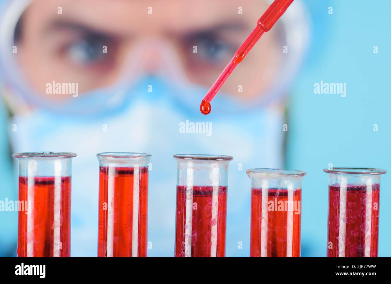 Arzt in einer Schutzbrille, der rote Flüssigkeit in die Reagenzgläser tropft. Blutprobe. Laborforschung. Stockfoto