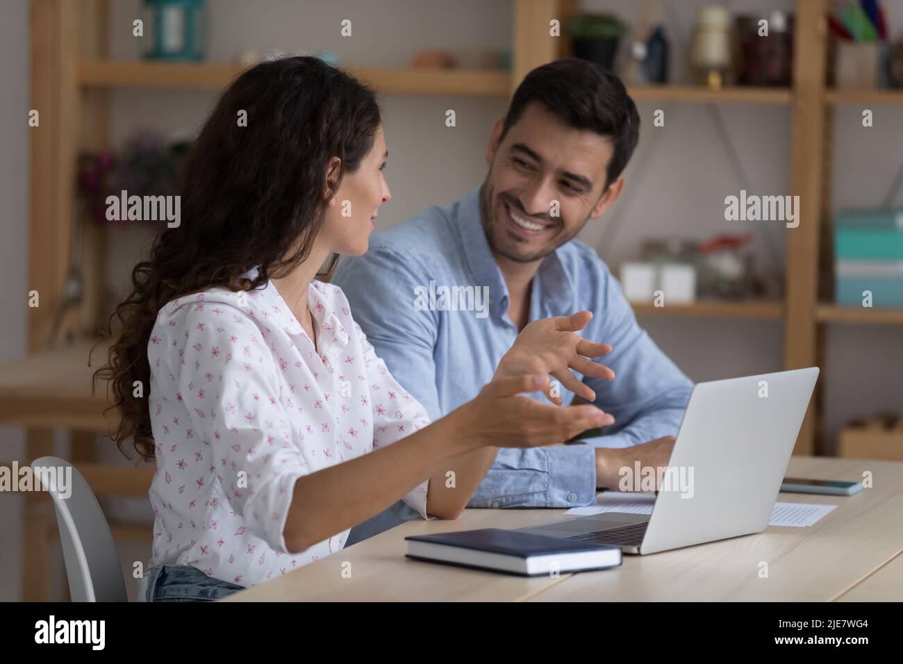 Hispanische Kollegen sitzen mit einem Laptop am Schreibtisch und diskutieren über Unternehmenssoftware Stockfoto