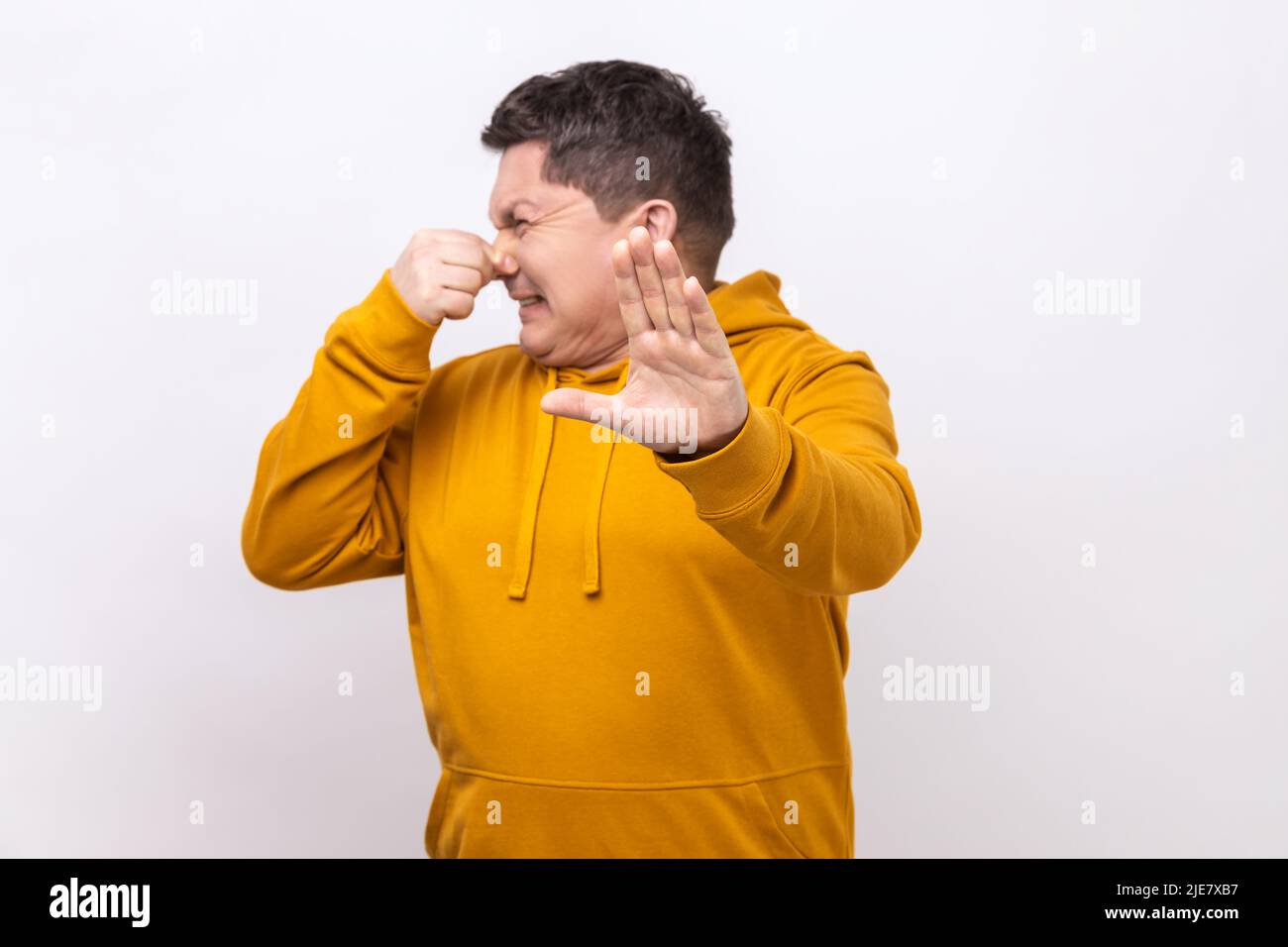 Stoppen Sie diesen schrecklichen Gestank. Mann, der vor Ekel grimacing, Ablehnung mit erhobener Handfläche zeigt, Nase kneift, um schlechten Geruch zu vermeiden, trägt einen Kapuzenpullover im urbanen Stil. Innenaufnahme des Studios isoliert auf weißem Hintergrund. Stockfoto