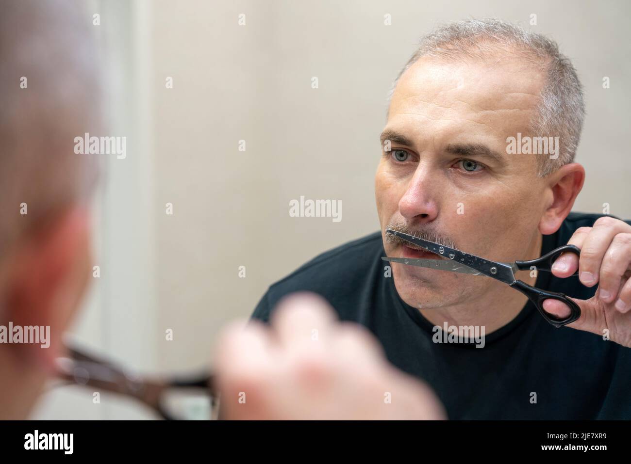 Gutaussehender Mann mittleren Alters, der mit einer Schere seinen Schnurrbart Schnitt Stockfoto