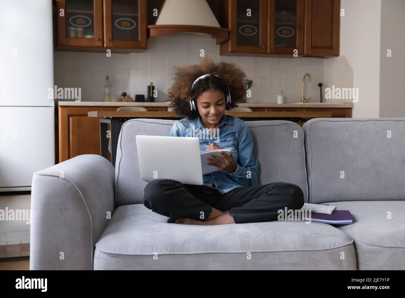Afrikanisches studentisches Mädchen in Kopfhörern, das zu Hause studiert, benutzt einen Laptop Stockfoto
