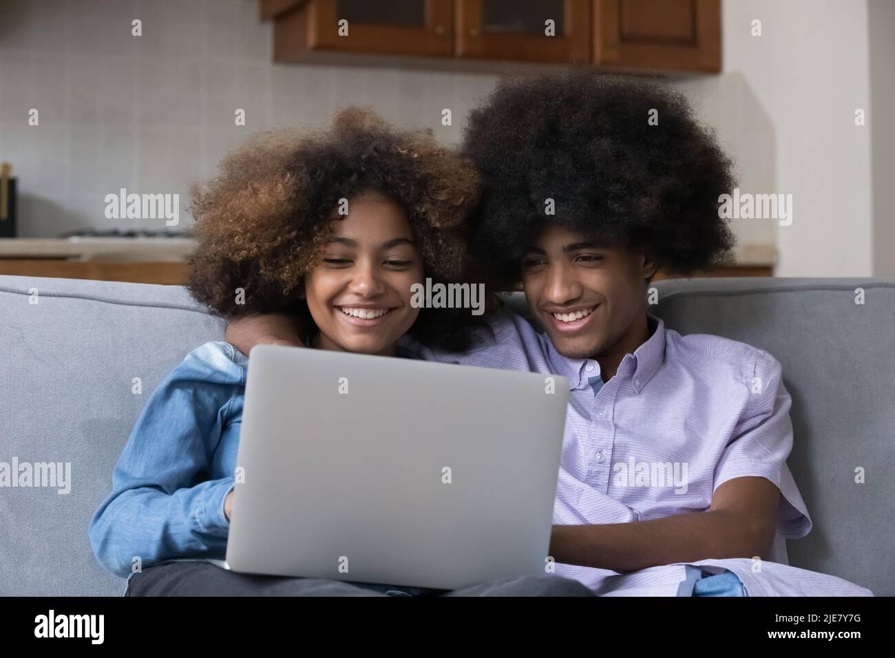 Fröhliches afrikanisches Teenager-Paar sitzt auf dem Sofa mit Laptop Stockfoto