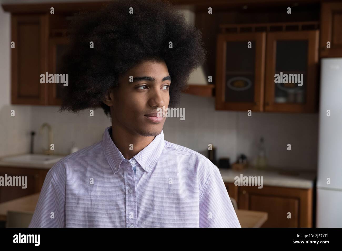 Ernst nachdenklicher afrikanischer Kerl, der in der heimischen Küche steht und beiseite starrt Stockfoto
