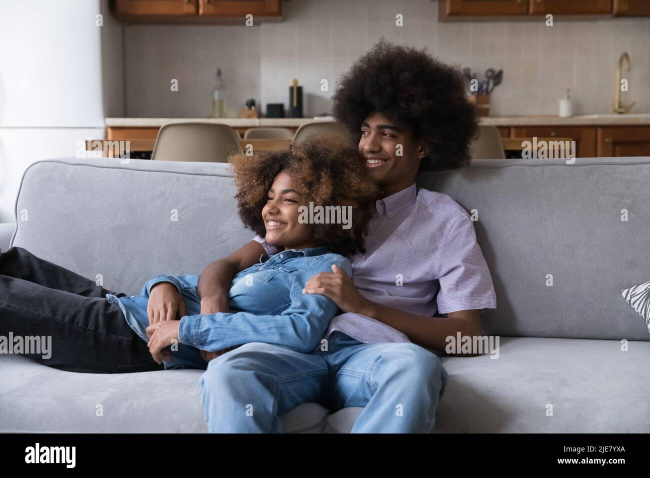 Afrikanisches Teenager-Paar, das sich auf dem Sofa entspannt und lächelnd in die Ferne starrt Stockfoto