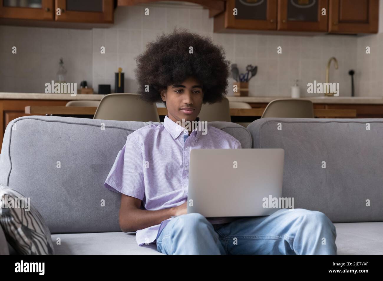 Afrikanischer Teenager sitzt auf dem Sofa und benutzt einen Laptop Stockfoto