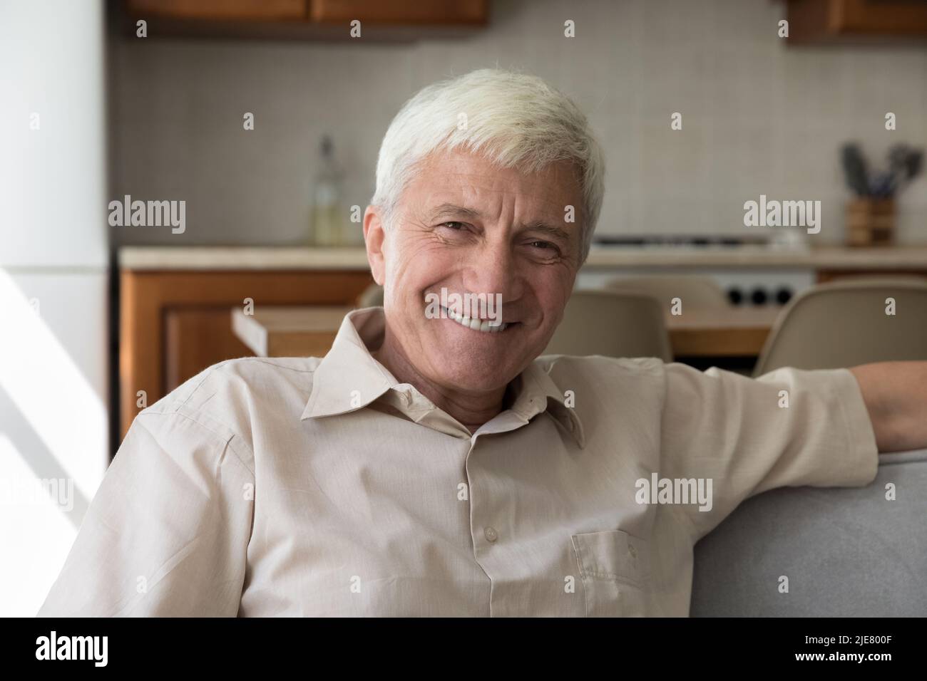Glücklicher älterer Mann, der sich auf dem Sofa entspannt und lächelt und die Kamera anschaut Stockfoto