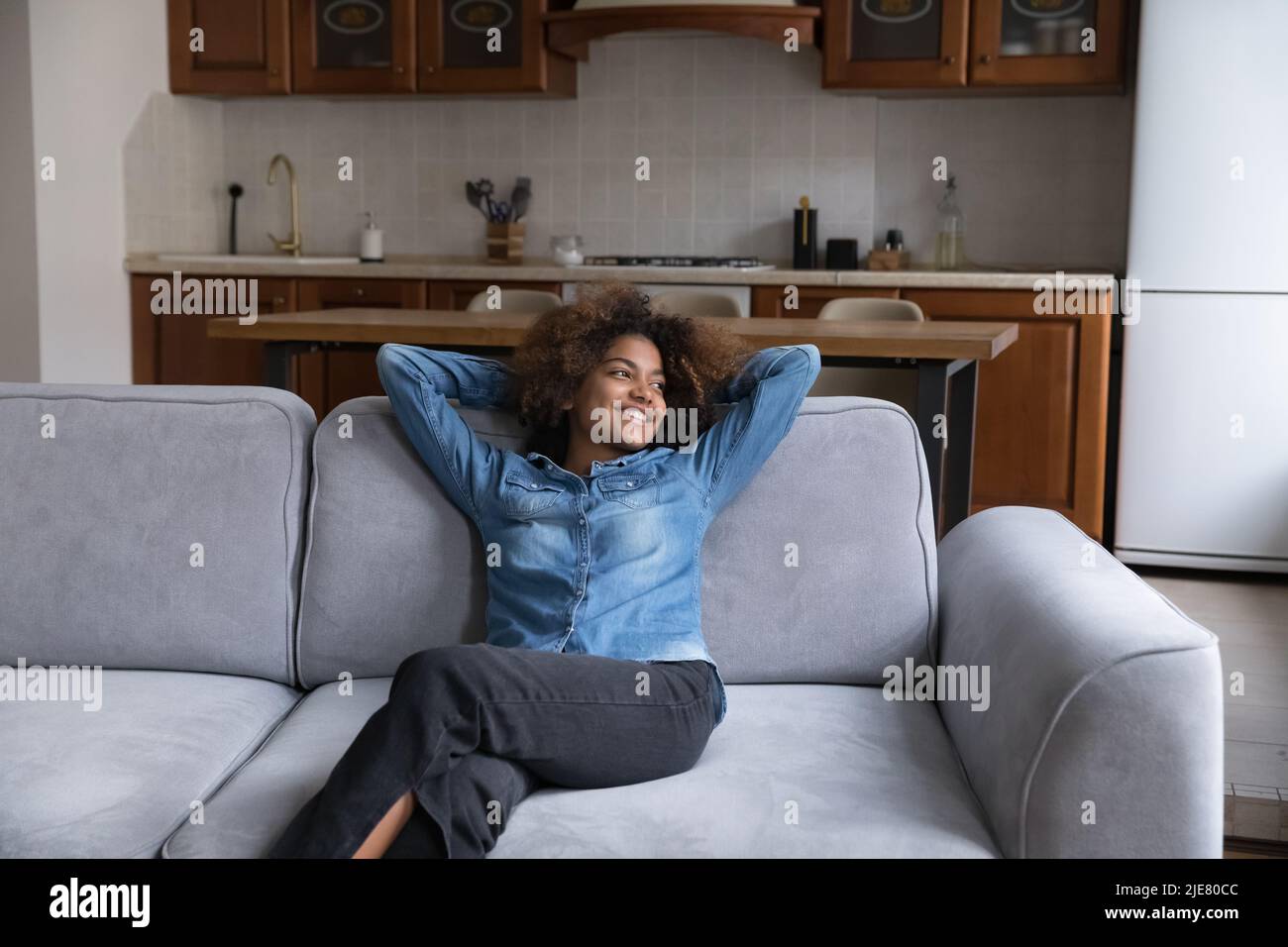 Afrikanisches Mädchen, das auf dem Sofa ruht, sieht verträumt aus und starrt in die Ferne Stockfoto