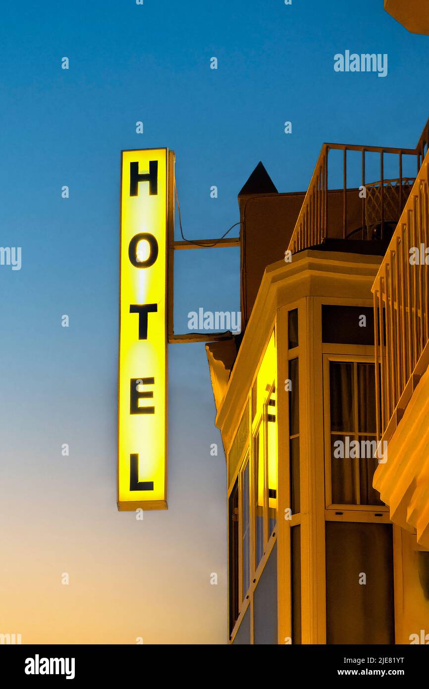 Ein hell erleuchtetes Hotelschild zeigt sich deutlich am Abendhimmel dahinter. Das Schild ist senkrecht und an der Vorderseite des Hotels angebracht. Stockfoto