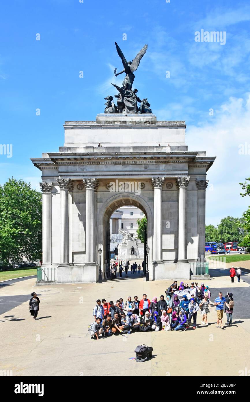 Touristen, die sich für ein Foto oder einen Film in einer großen Gruppe vor dem historischen Wellington Arch und der Quadriga Hyde Park Corner London England, Großbritannien, positionieren Stockfoto