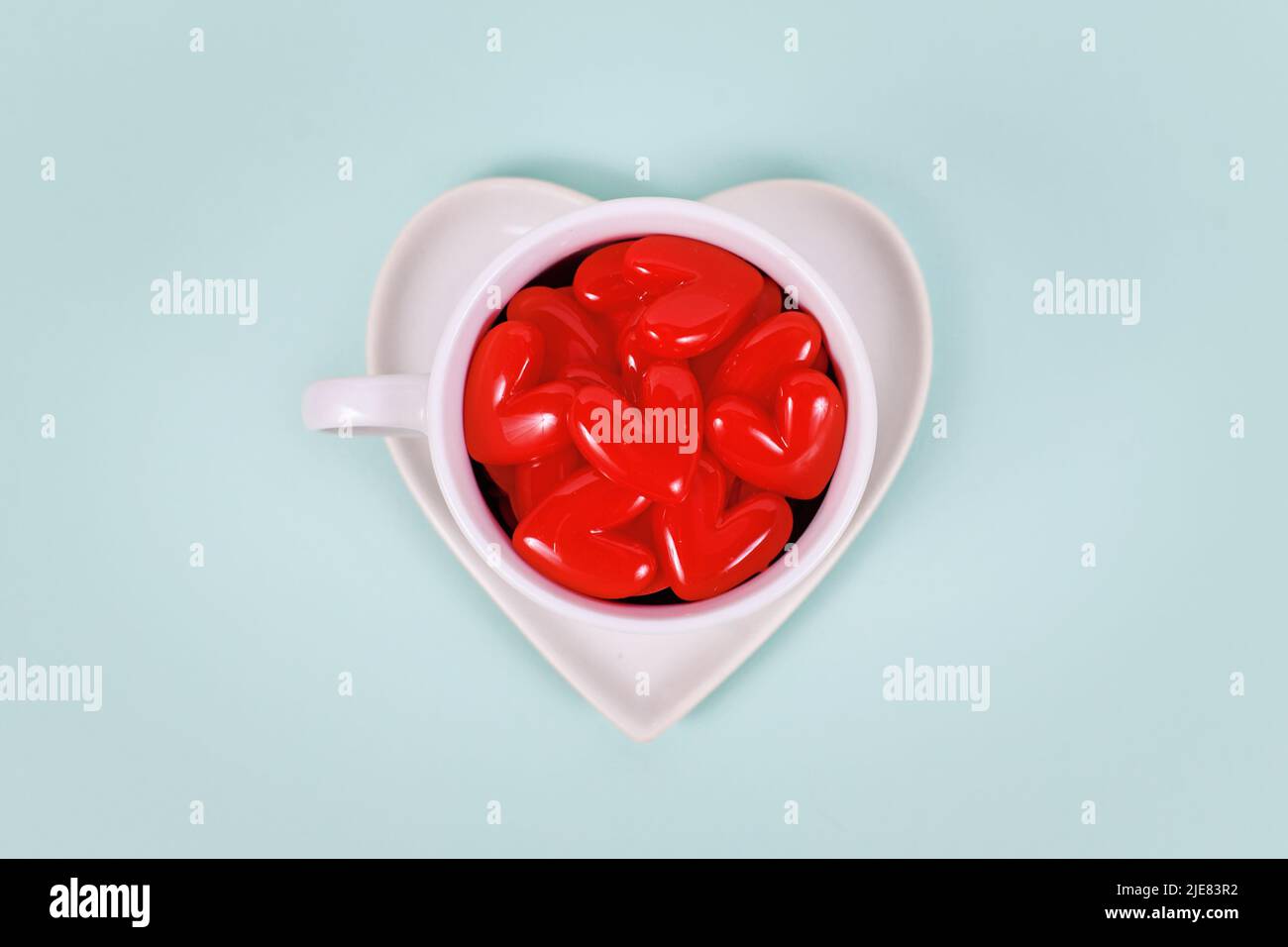 Rote Herzverzierungen in weißer Teetasse auf mintgrünem Hintergrund Stockfoto