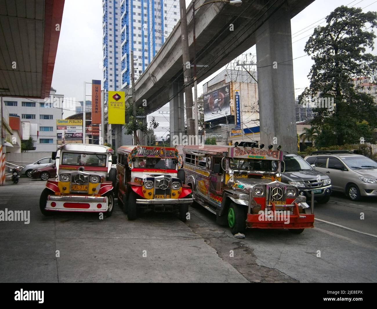 Jeepneys, die auf dem Vorplatz einer Tankstelle mit U-Bahn-Überflug über Quezon City geparkt sind, Stockfoto