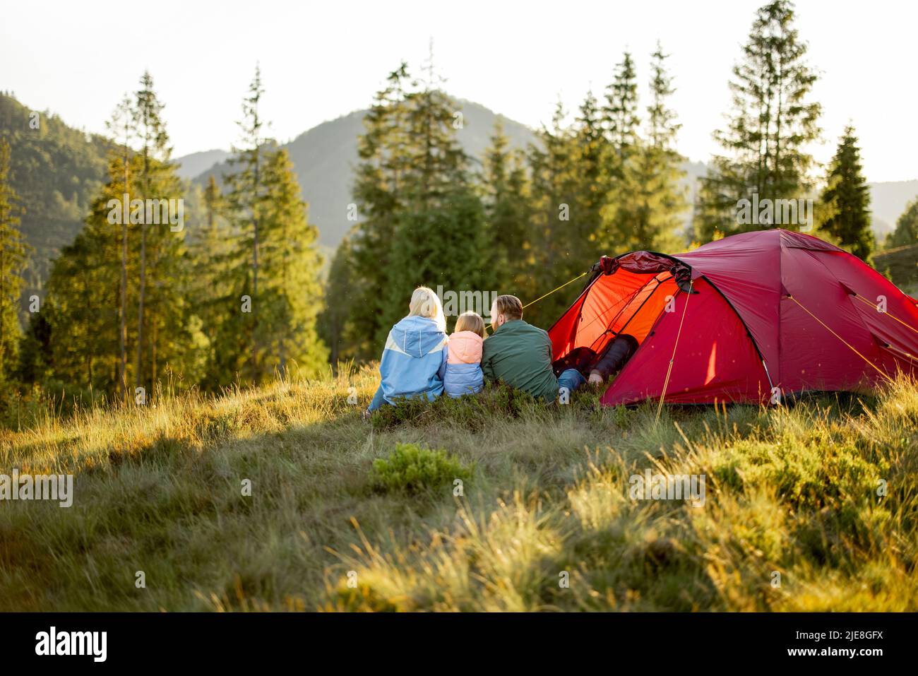 Familie mit Kind sitzt zusammen auf dem Campingplatz in der Nähe des Zeltes in den Bergen Stockfoto