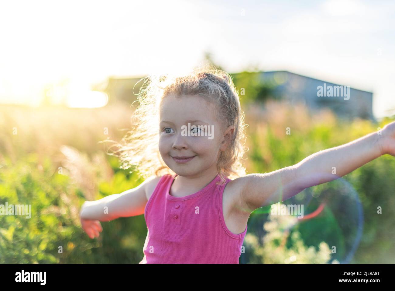 Kleine fröhliche blonde Mädchen vor dem Hintergrund von Gras und Sonnenuntergang Stockfoto