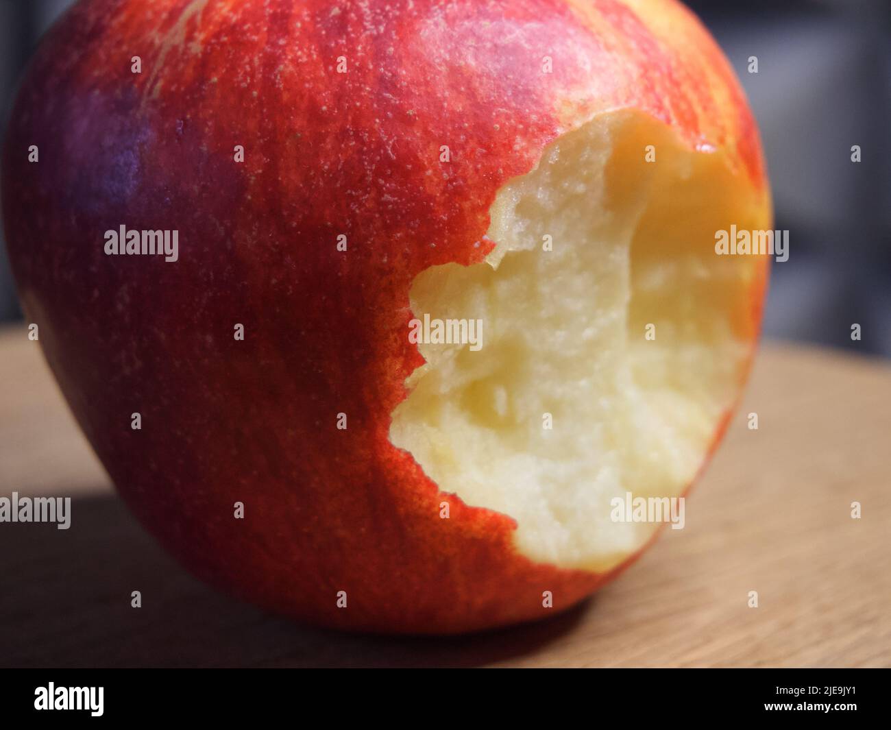 Ein gebissenen roten Apfel auf einer hölzernen Oberfläche. Makro „Reifer Apfel“. Stockfoto
