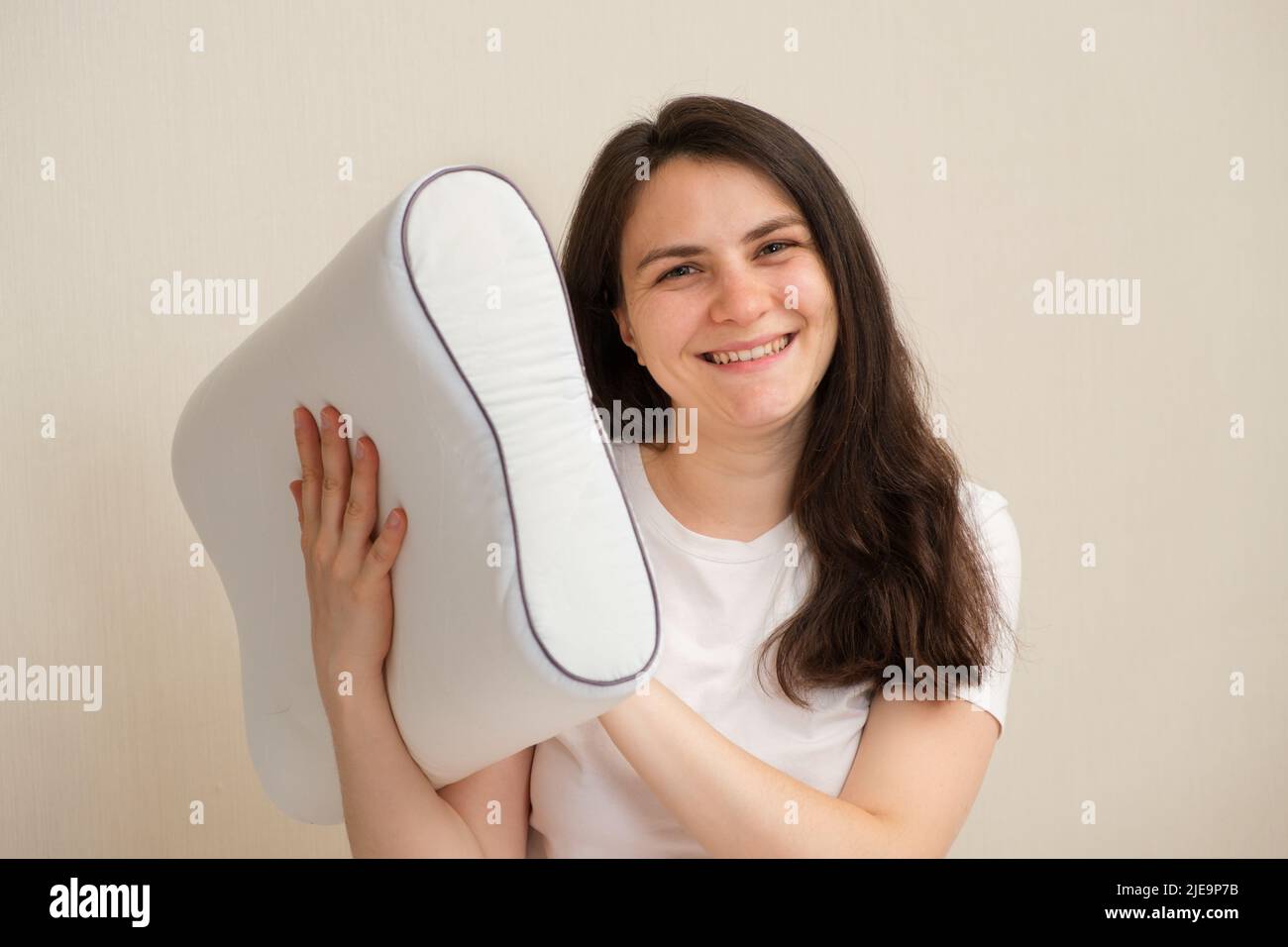 Eine Frau hält ein orthopädisches Kissen aus Memory Foam und lächelt. Auswahl des richtigen Kissens für einen gesunden Schlaf Stockfoto