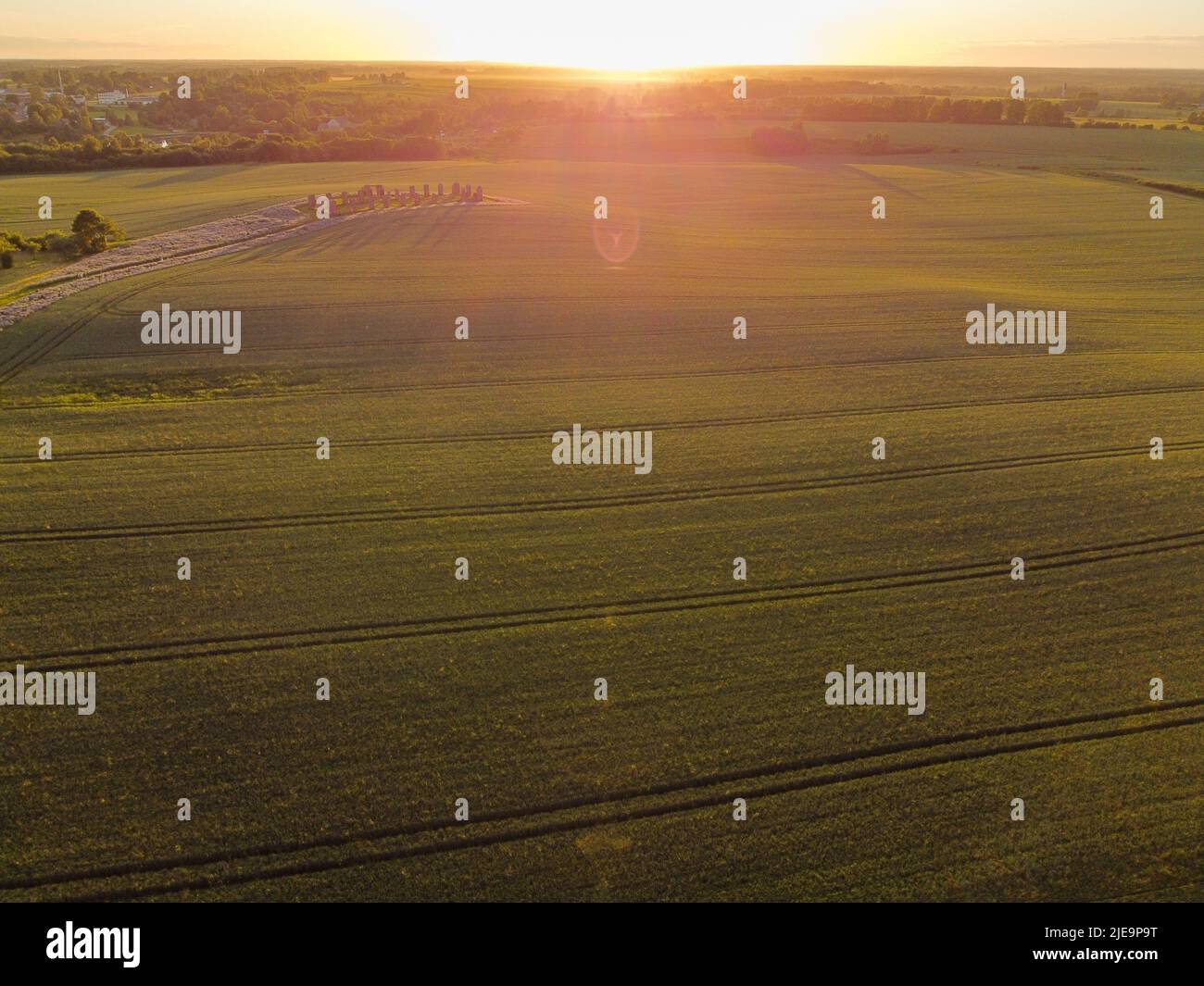 Luftaufnahme mit wunderschönem Getreidefeld bei Sonnenuntergang mit einem riesigen Steinhaus in der Mitte des Feldes. Das Gebäude ähnelt stonehenge. Smiltene ston Stockfoto